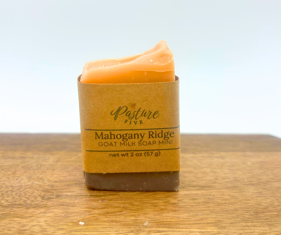 Mini Goat milk soap bar in a brown paper wrap on a wooden surface with a light blue background
