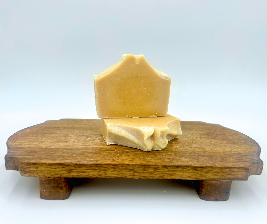 Two pieces of goat milk soap with a simple design on a wooden stand with a white background
