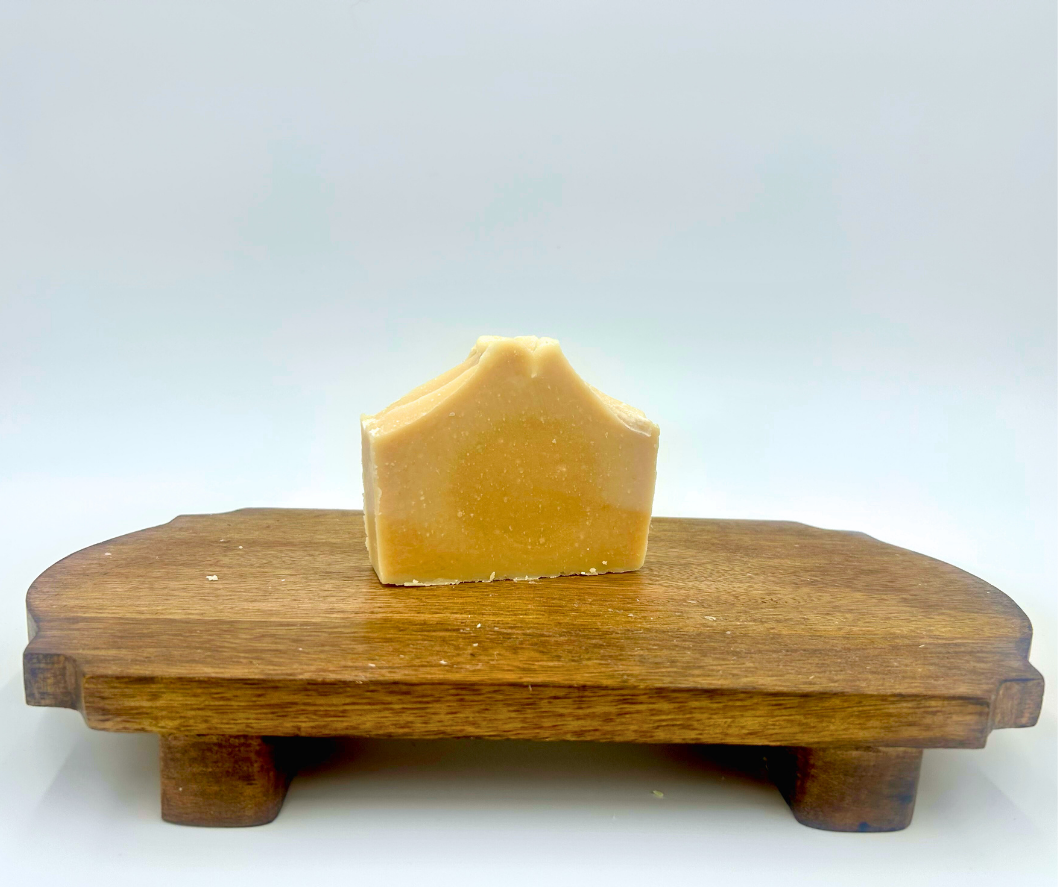 Bar of goat milk soap on a wooden stand against a white background