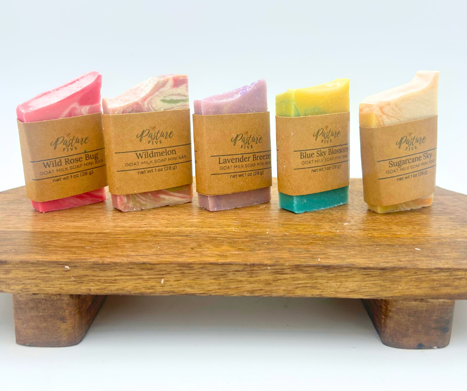 Five bars of soap in various colors on a wooden stand with a white background