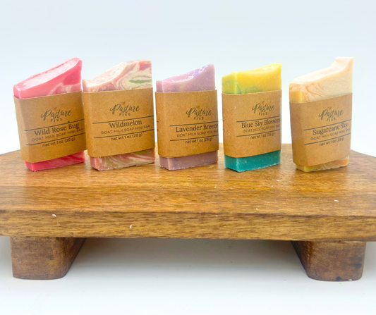 Five bars of soap in various colors on a wooden stand with a white background