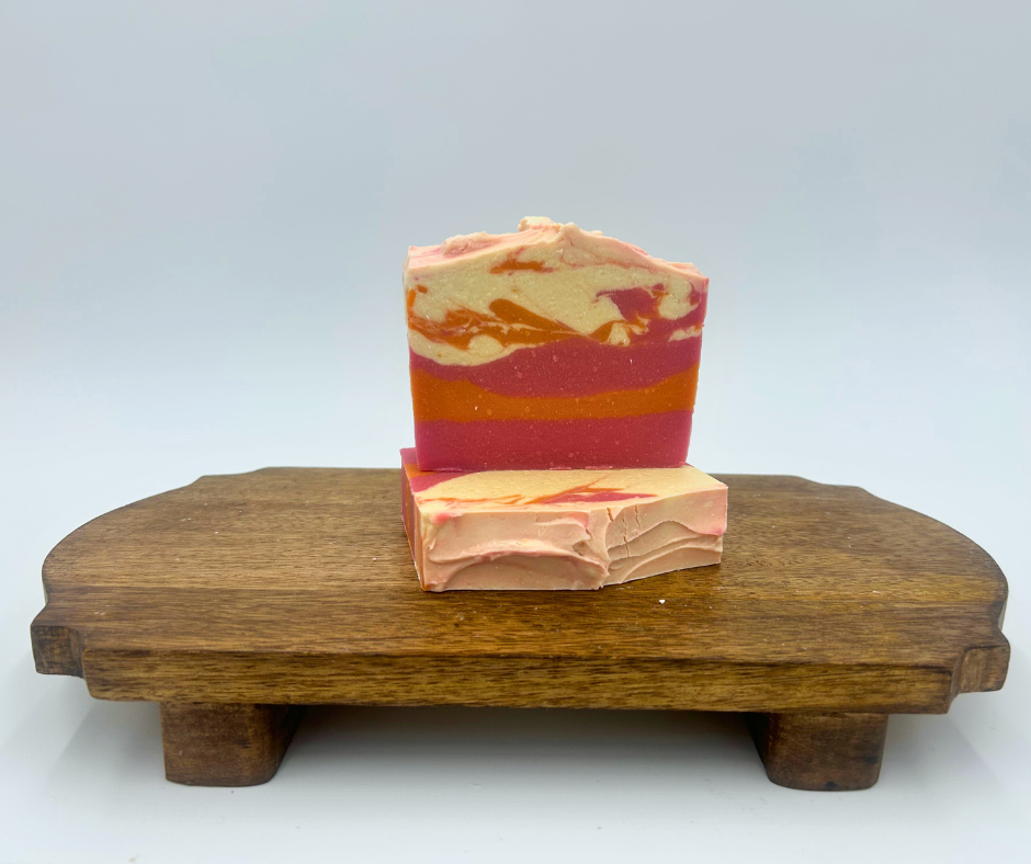 Two bars of multicolored soap stacked on a wooden stand against a light gray background
