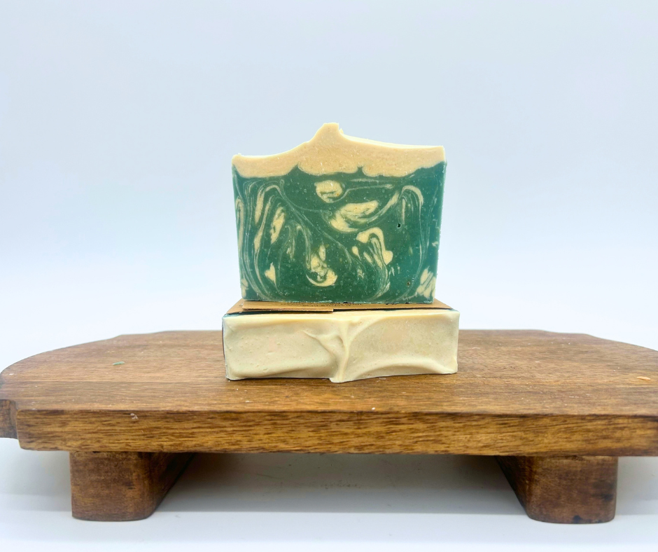 Two bars of Snowy Spruce goat milk soap bars on a wood board. 