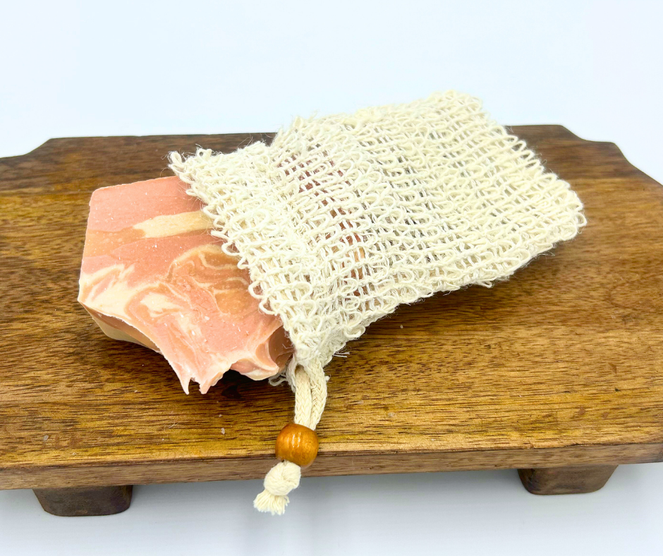 Pink soap bar with a natural fiber soap bag on a wooden block