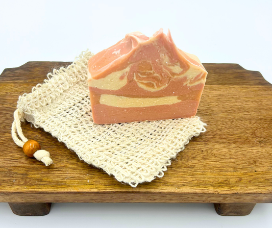 Bar of soap on a wooden surface with a natural fiber soap bag.