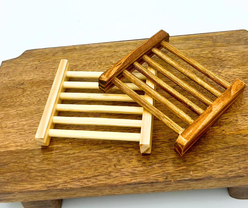 Two Wooden soap holders on a wooden surface. One with light wood and one with darker wood. 