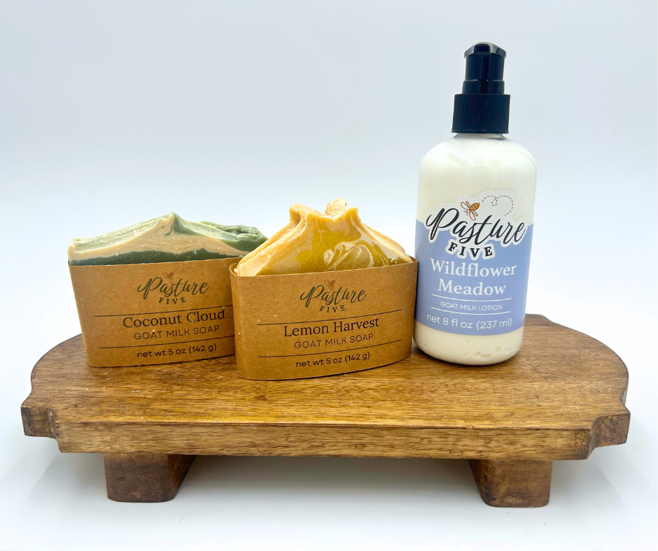 Three soap bars and a bottle of soap on a wooden stand with 'Pasture Five' branding.