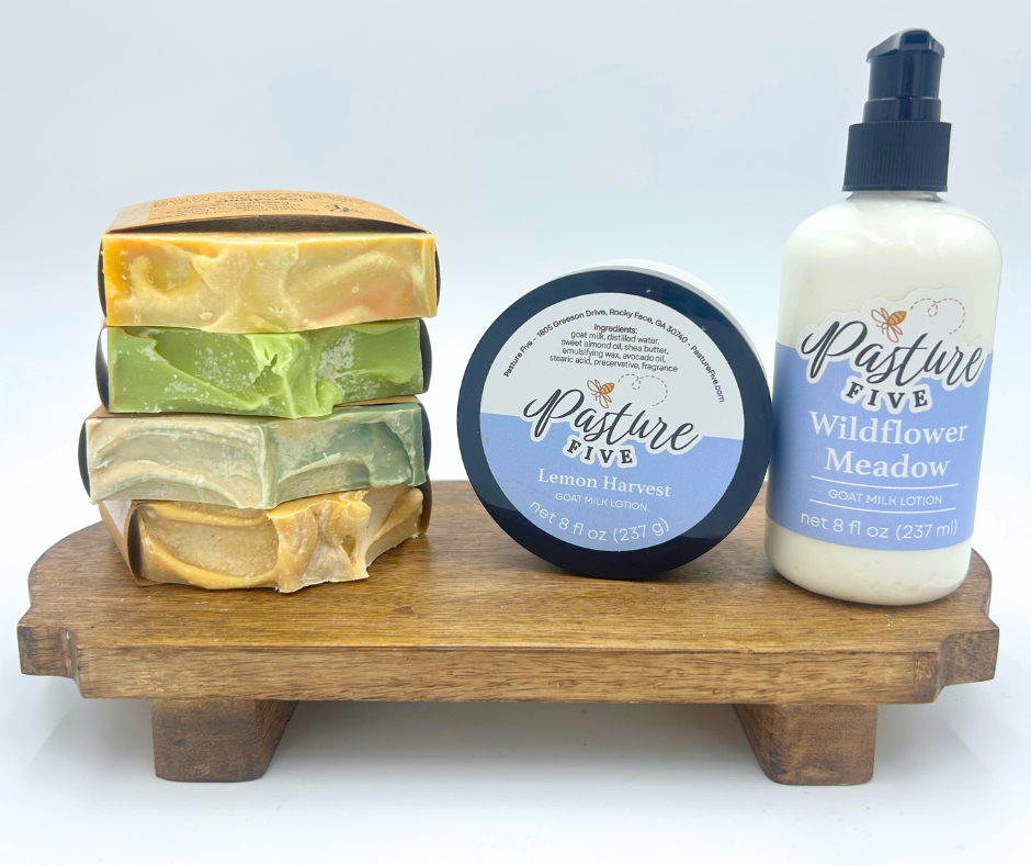 Stack of soap bars, a jar, and a bottle of lotion on a wooden stand with 'Pasture Five' branding.
