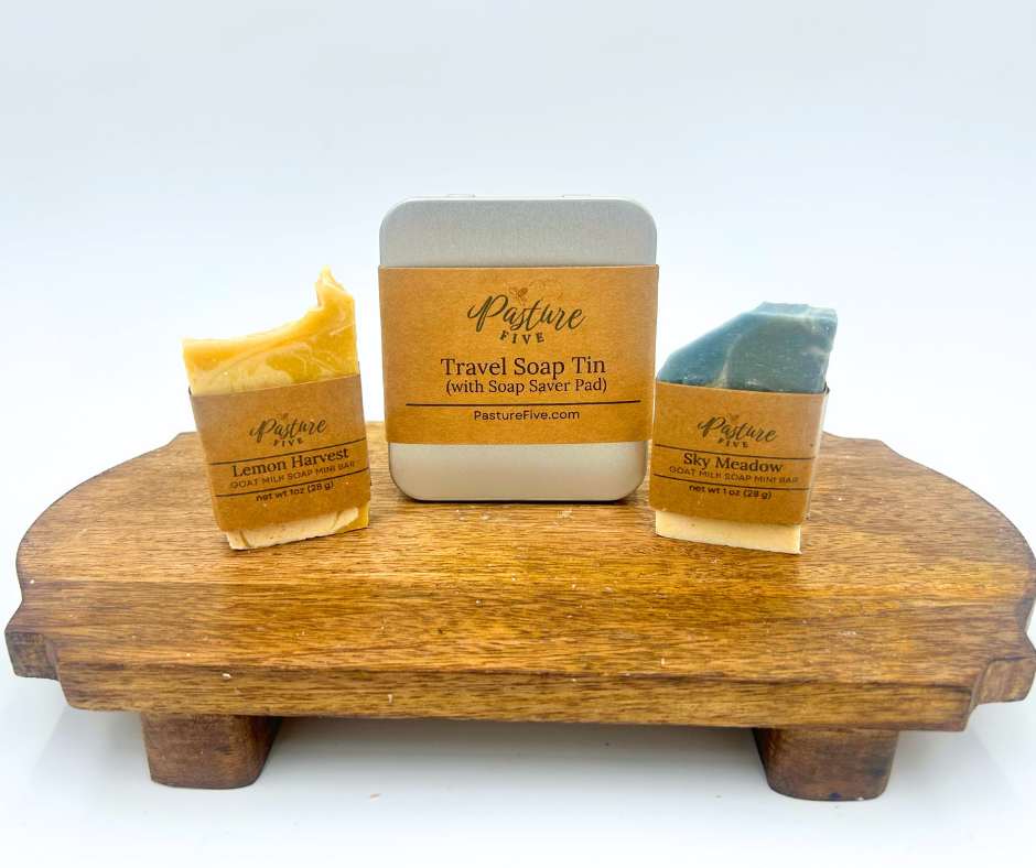 Pasture Five soap products including a travel soap tin and two bars of soap on a wooden stand with a white background.