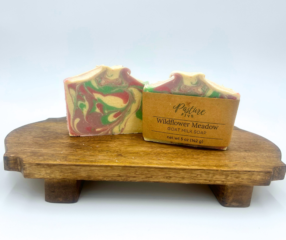 Two Wildflower Meadow Goat Milk soap bars on a wooden stand with a white background