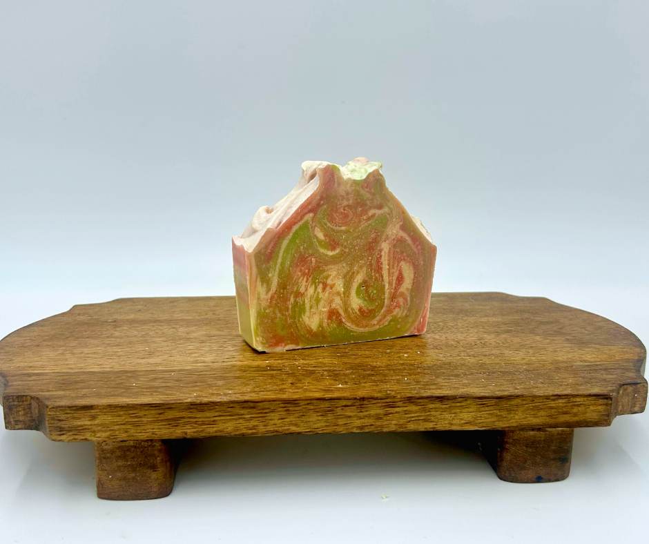 Decorative soap bar with green and pink pattern on a wooden stand against a white background
