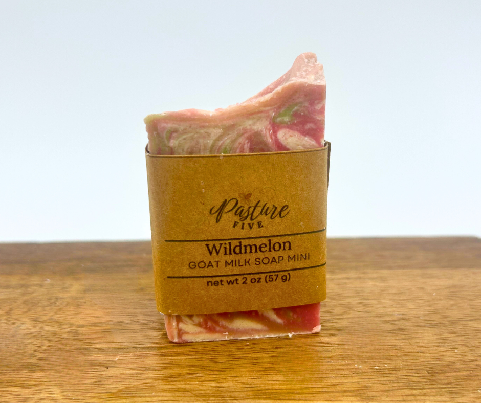 Mini Bar of soap with a floral design in a brown paper sleeve on a wooden surface.