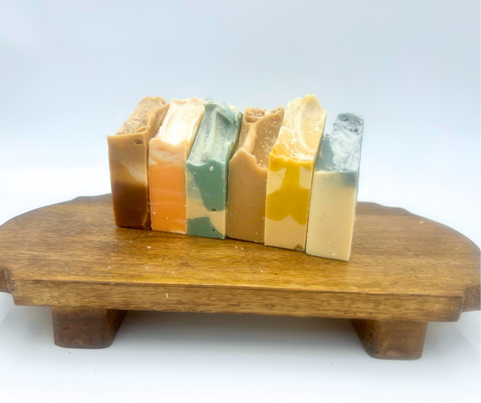 six colorful bars of goat milk soap on a wooden stand with a white background